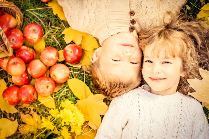 Two children lying in autumn leaves with apples