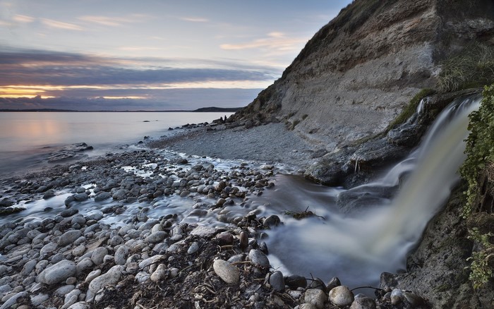 Waterfall cascading onto a rocky shore at sunset