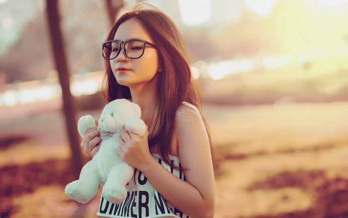 Young Asian girl with glasses holding a teddy bear