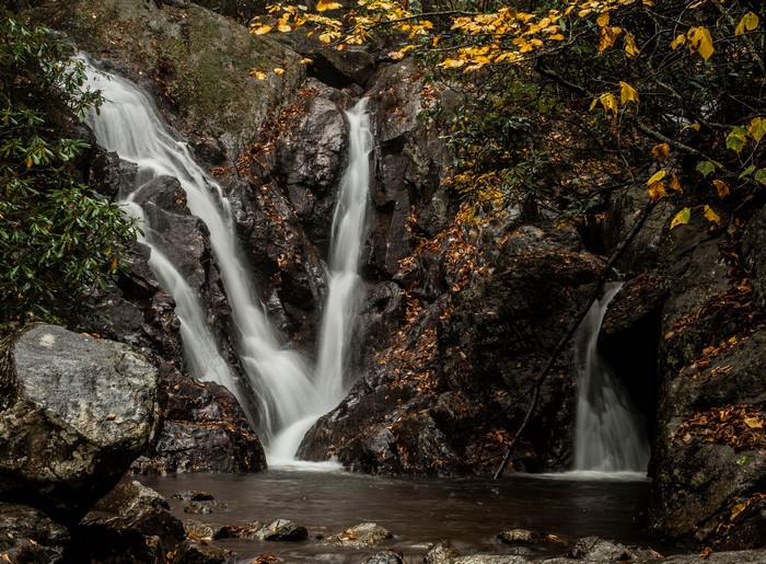 Waterfall cascading over dark rocks with autumn leaves