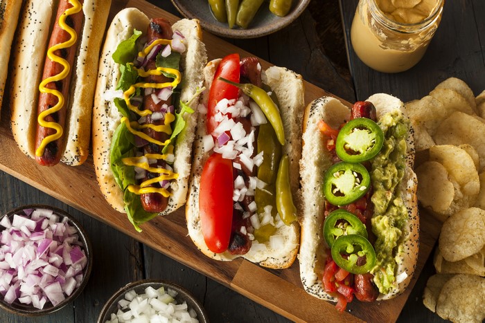 Four gourmet hot dogs with various toppings and chips