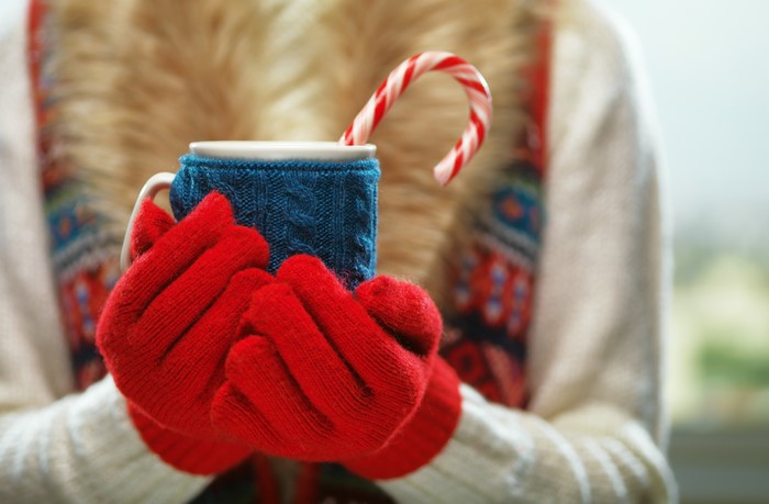 Hands in red gloves holding a mug with candy cane