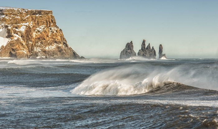 Waves crashing near snowy cliffs and sea stacks
