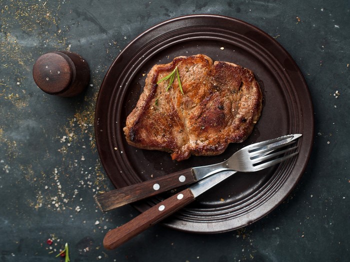 Cooked steak on a plate with fork and salt shaker