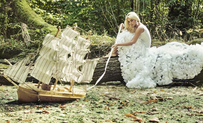 Blonde girl in white dress with model ship in forest