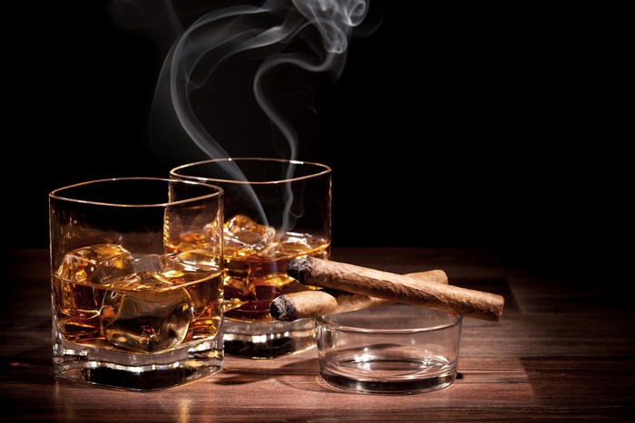 Two glasses of whiskey with cigars and smoke