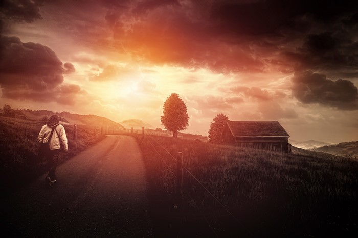 Person walking on a road towards sunset with a house