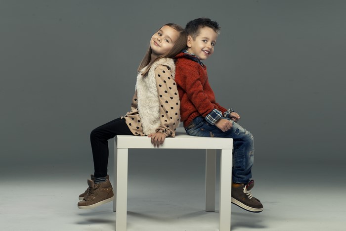 Two children sitting back to back on a white table