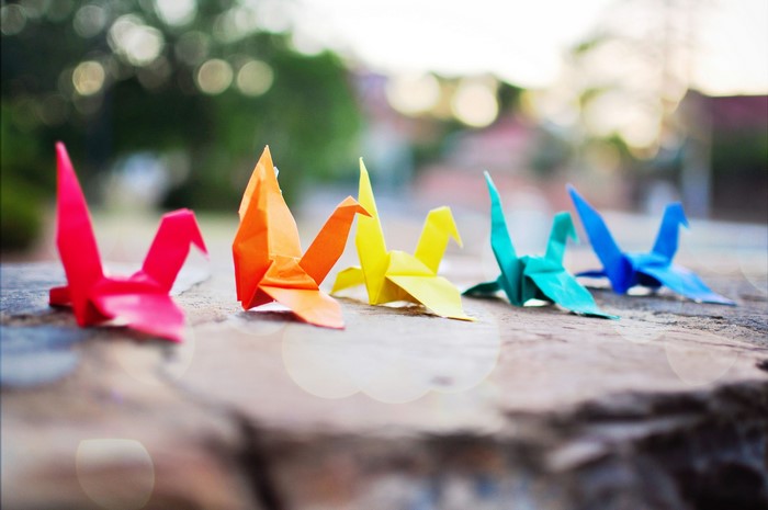 Origami cranes in a rainbow of colors on a stone surface