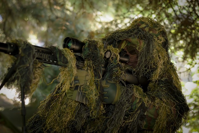 Sniper in camouflage aiming rifle