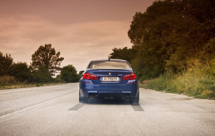 Blue BMW M5 F10 doing a burnout on a road