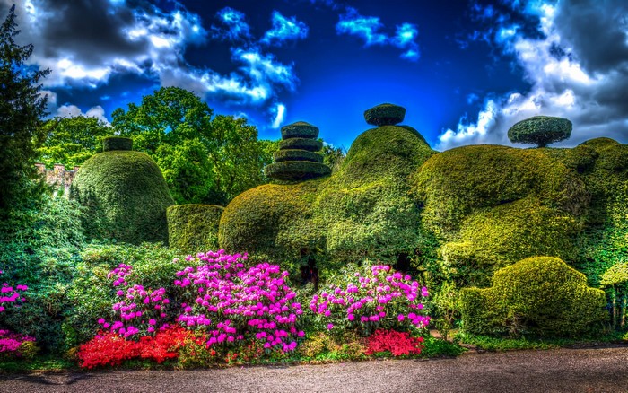 Topiary garden with pink and red flowers under a dramatic sky
