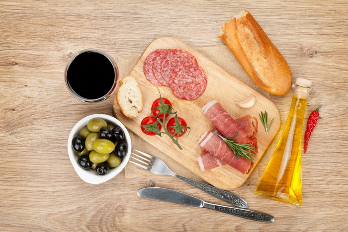 Charcuterie board with salami, ham, olives, tomatoes, bread, and wine