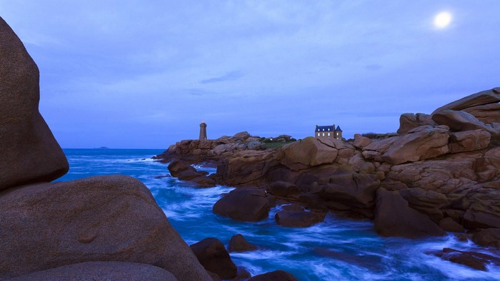 Lighthouse and house on rocky coast at dusk