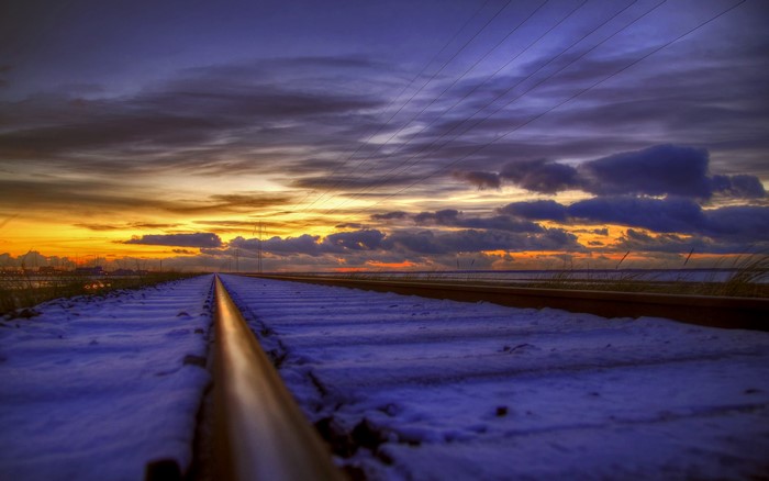 Railroad tracks covered in snow at sunset with clouds