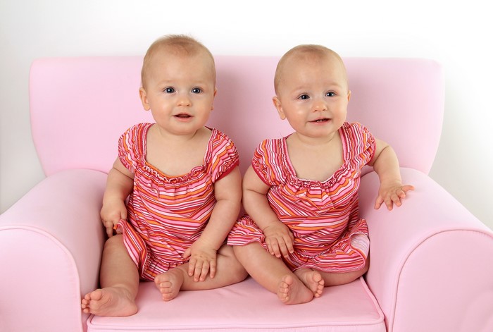 Two babies in pink dresses on a pink armchair
