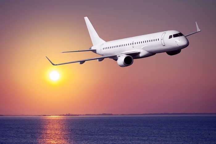 Airplane flying over the ocean at sunset