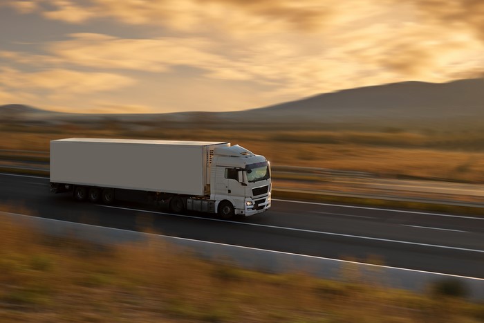 White semi-truck driving on a highway at sunset