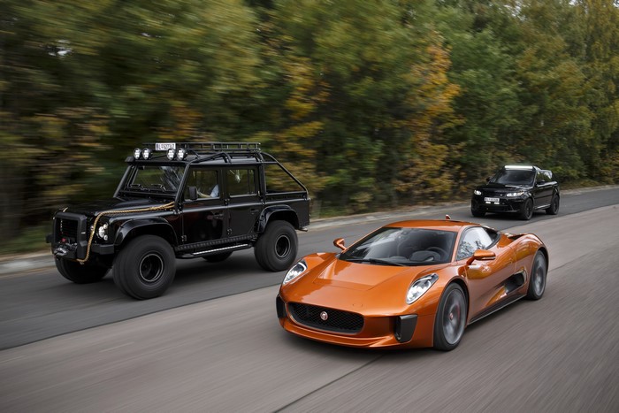 Jaguar C-X75 and two black SUVs on a road