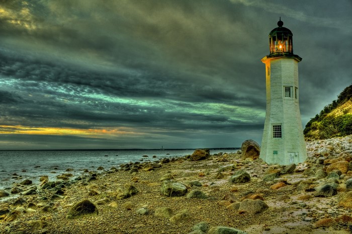 White lighthouse on a rocky shore under a stormy sky