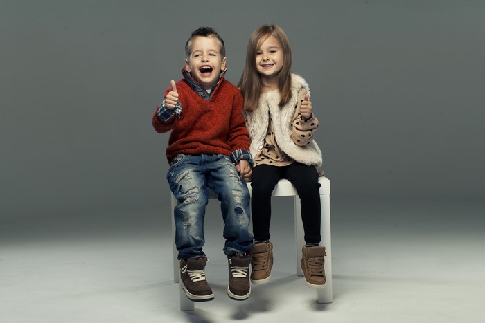 Two children in sweaters and jeans giving thumbs up