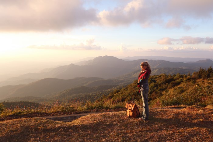 Woman with backpack on mountain overlook at sunset