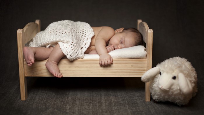 Baby sleeping in a wooden bed with a toy sheep