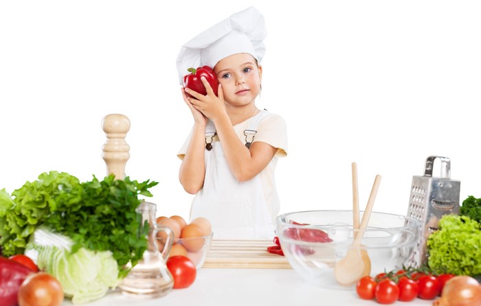 Little girl in chef uniform holding red bell pepper
