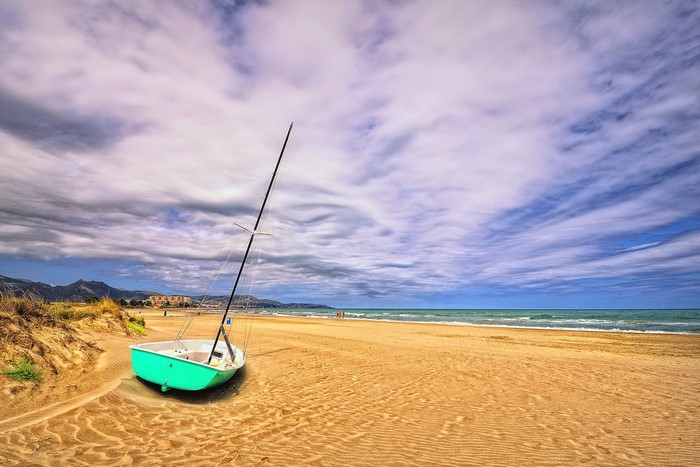 Sailboat on a sandy beach with cloudy sky