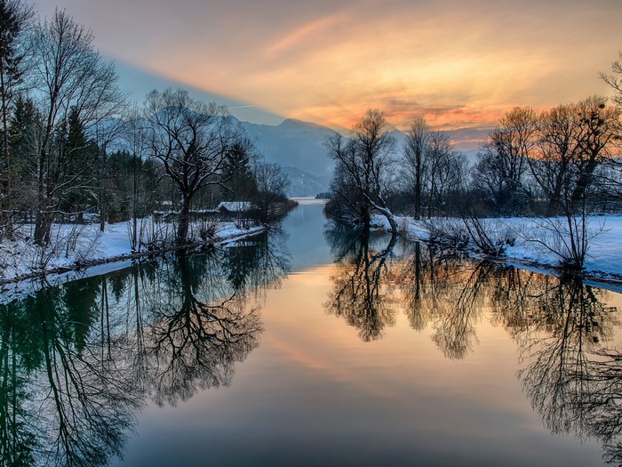 Winter river reflecting trees and mountains at sunset