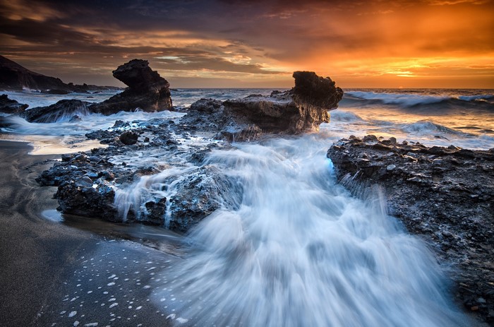 Waves crashing on rocky coast at sunset in Spain