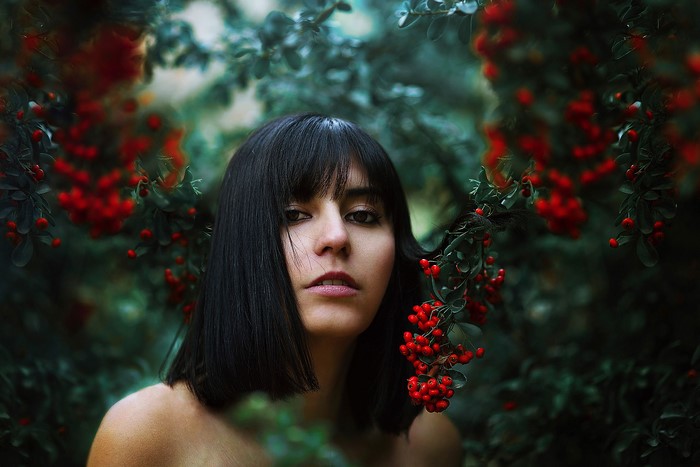 Brunette girl with black hair and bangs surrounded by red berries