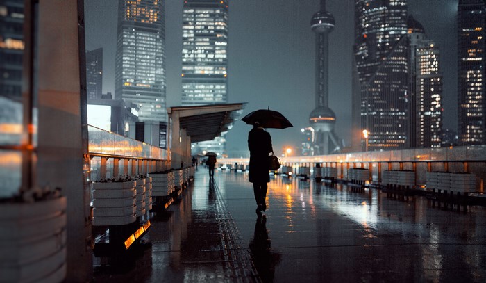 Person with umbrella walking on wet street in Shanghai at night