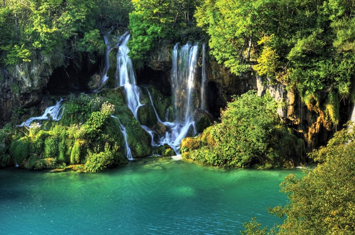 Waterfalls cascading into a turquoise lake surrounded by lush green forest