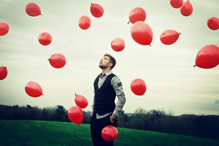 Man looking up at red balloons in a field