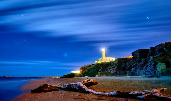 Lighthouse on a cliff at night with a driftwood log