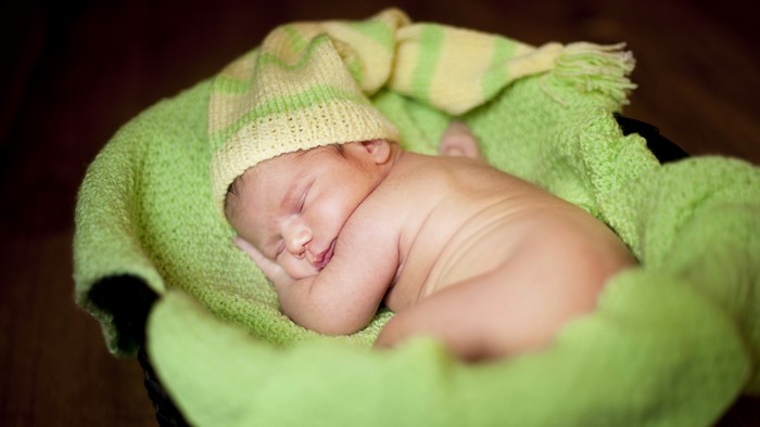 Newborn baby sleeping in a green blanket and hat