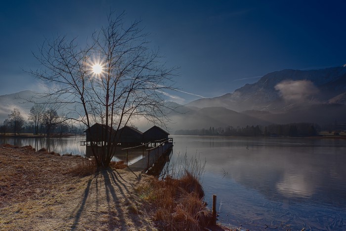 Boathouses on a frozen lake with mountains and sun