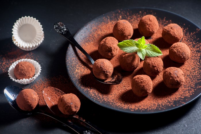 Chocolate truffles dusted with cocoa powder on a plate and spoons