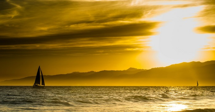 Sailboats on the ocean at sunset with mountains