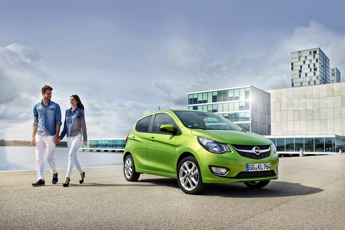 Couple walking by a green Opel Karl with modern buildings