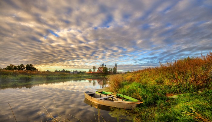 Boats on a river with a village and temple under cloudy sky