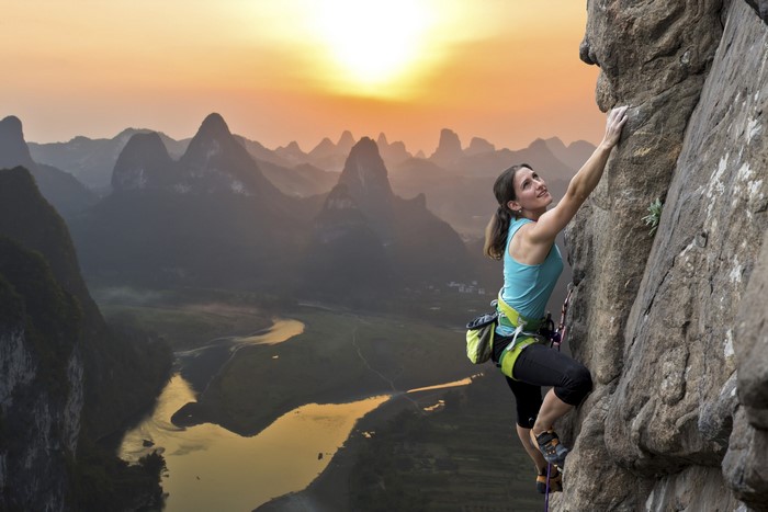Woman rock climbing with mountains and river at sunset
