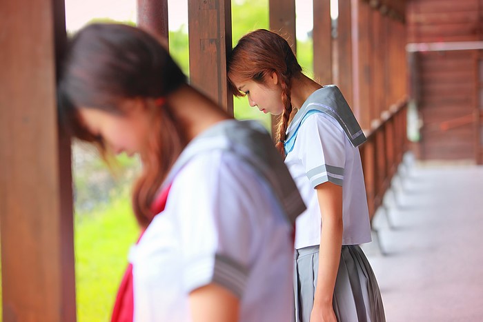 Two Asian schoolgirls leaning on a wooden pillar