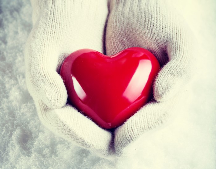 Hands in mittens holding a red heart in snow