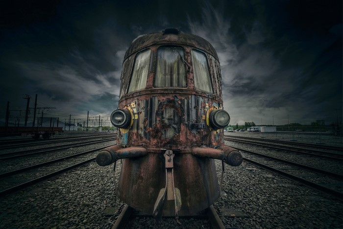 Abandoned rusty locomotive on train tracks under stormy sky