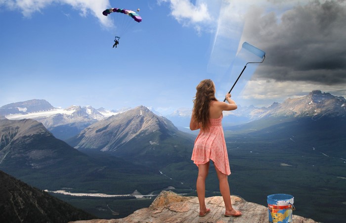 Woman painting the sky over mountains with a parachute