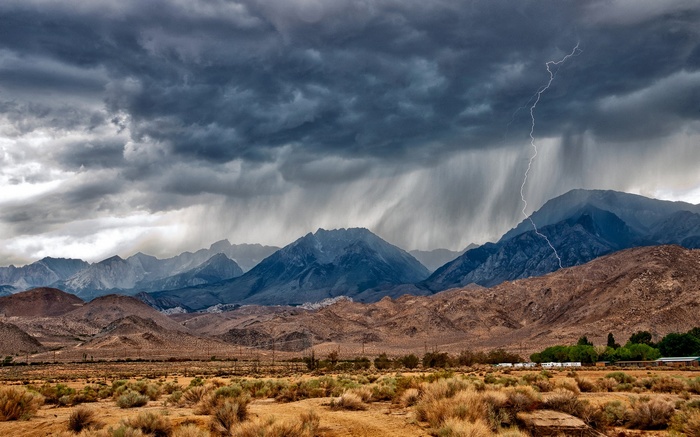Stormy mountains with lightning and rain over desert landscape