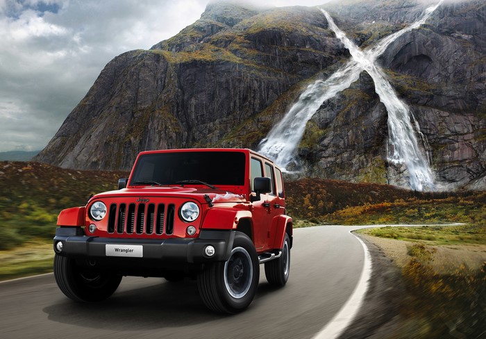 Red Jeep Wrangler driving on a road with waterfalls and mountains