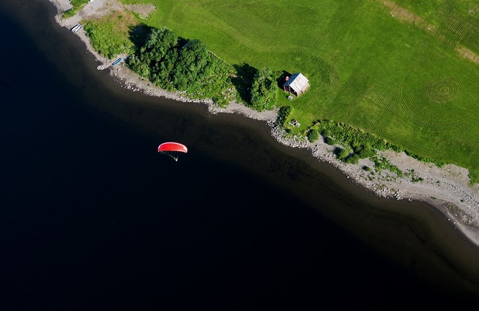 Paraglider flying over a dark lake near a grassy shore